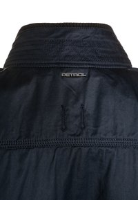 Dark navy jacket collar with stitched details and small "PETROL" metal logo centered below collar seam.