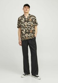 Chemise à manches courtes avec un motif floral en beige et noir, ornée de grandes fleurs et feuilles. Associée à un pantalon noir ajusté et des baskets noires.
