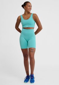Een twee-delig sportset in lichtturquoise, bestaande uit een cropped tanktop en high-waisted shorts, gemaakt van een rekbare, geribbelde stof.