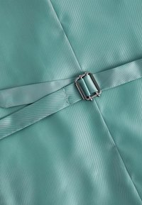 Gros plan d'une boucle en métal argenté fixant deux sangles en satin bleu turquoise clair superposées avec des coutures visibles.