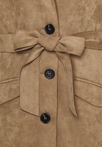 Brun mockakappa med knytband i midjan, två framfickor och svarta knappar. Mjuk textur med en slät finish.