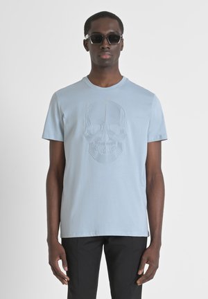 Camiseta de algodón azul claro con un diseño de calavera texturizado en la parte frontal, con cuello redondo y mangas cortas, combinada con pantalones negros.