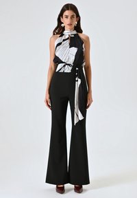 Pantalons noirs évasés avec une taille ajustée associés à un débardeur noir et blanc à motifs sans manches avec un lien. Texture de tissu lisse.