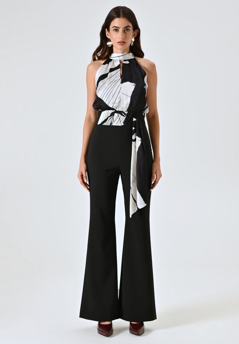 Pantalons noirs évasés avec une taille ajustée associés à un débardeur noir et blanc à motifs sans manches avec un lien. Texture de tissu lisse.
