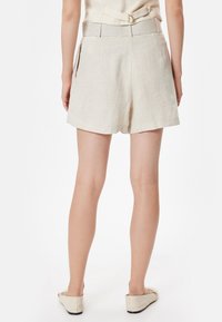 Pantalones cortos de lino beige con una cinturilla ancha, bolsillos laterales y un ajuste relajado. Textura suave y un diseño simple y limpio.