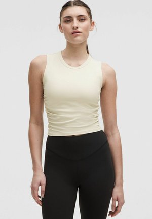 Geripptes, hellgelbes ärmelloses Oberteil mit figurbetonter Silhouette, kombiniert mit hoch taillierten schwarzen Leggings. Glatte Textur, minimalistisches Design.