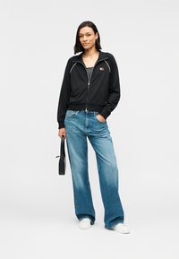 Μαύρο μπουφάν με φερμουάρ και λευκή διακόσμηση, σε συνδυασμό με ανοιχτό μπλε τζιν με φαρδιά μπατζάκια. Η εμφάνιση ολοκληρώνεται με λευκά παπούτσια και μια μικρή μαύρη τσάντα.