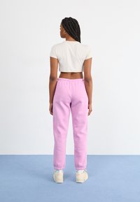 T-shirt cropped beige clair et pantalon de survêtement rose avec des poignets élastiques, présentant une texture lisse. Les chaussures sont des baskets crème.
