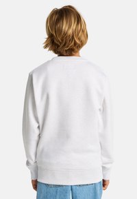 Felpa bianca realizzata in un morbido tessuto, con collo a giro e polsini a coste. Il retro presenta un piccolo etichetta, abbinata a jeans azzurri chiari.