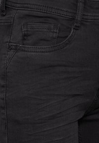 Svarta denimjeans med en texturerad yta, en liten framficka och standardstickningar längs sömmarna.