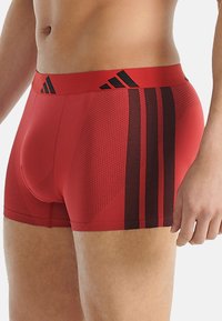 Červené boxerky vyrobené z pružného materiálu, s černými akcenty a texturovaným vzorem. Elastický pas s detailním logem.