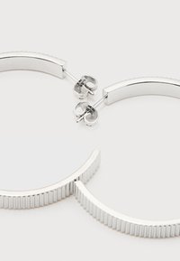 Ζευγάρι ασημένια σκουλαρίκια κρίκοι με ραβδώσεις και κούμπωμα πεταλούδα σε λευκό φόντο.