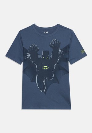 Sötétkék póló, amelyen egy Batman repül előre, világító szemekkel és a mellkasán lévő logóval, a bal ujján pedig GAP logóval.