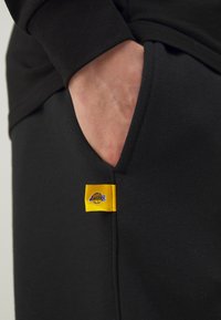 Sorte joggebukser med en gul Lakers-logo på lommen, laget av myk stoff med avslappet passform og sidelommer.
