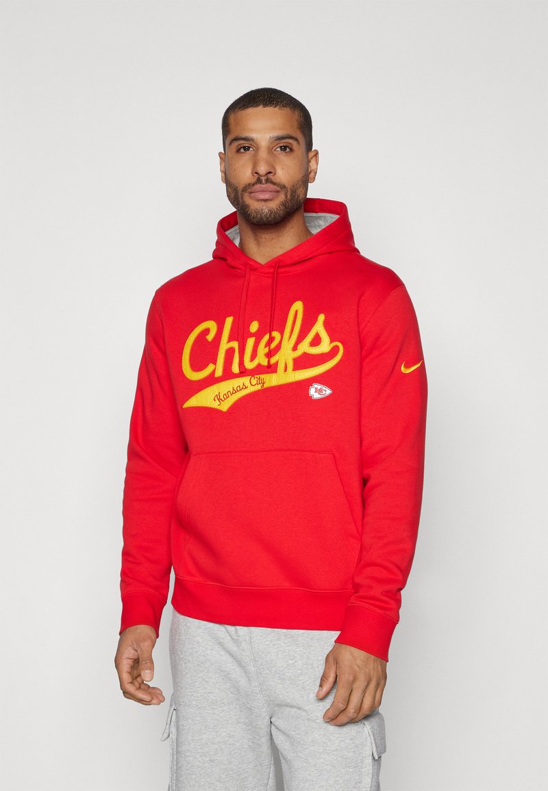 Raudona dėvimoji striukė su užrašu „Chiefs“ geltonu script stiliumi, tekstas „Kansas City“, priekinė kišenė ir „Nike“ logotipas ant rankovės. Medvilnės mišinys su minkštu paviršiumi.