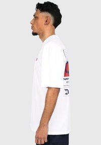 White cotton t-shirt with short sleeves, featuring a graphic print in red and navy on the back and a small logo on the front.