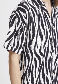Camicia a maniche corte in bianco e nero con motivo a strisce zebra, con colletto e tre bottoni sul davanti.