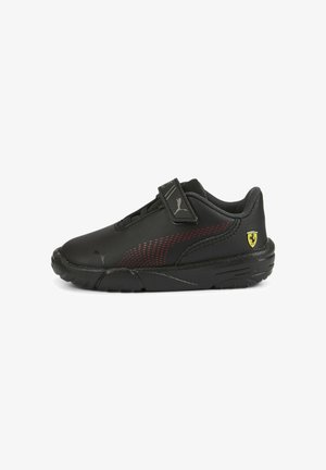 Chaussures de sport noires avec une tige synthétique lisse, des accents rouges, une bride auto-agrippante et une semelle en caoutchouc texturée. Logo Ferrari sur le talon.