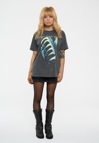 Graphic t-shirt in dark gray featuring a blue and white design. Paired with a black denim skirt and tall black boots with buckle accents.