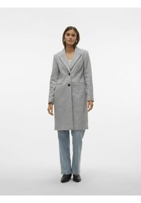 Cappotto in misto lana grigio con maniche lunghe, revers a punta, design a un solo petto, due tasche frontali e bottoni neri. Indossato sopra un jeans chiaro.