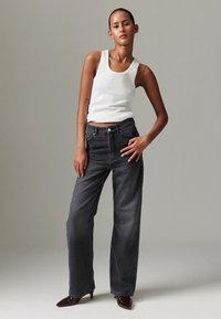 Crne traperice s visokim strukom s opuštenim krojem, s klasičnim dizajnom s pet džepova i suptilnim bljeđenjem. Uparene s bijelim topom na bretele.