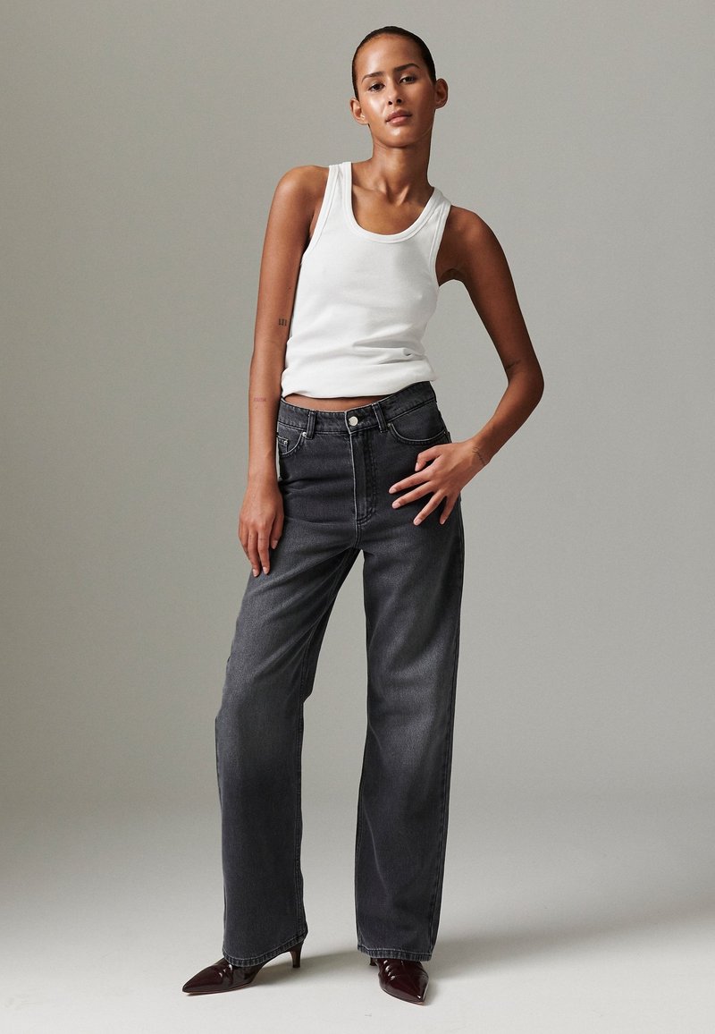 Crne traperice s visokim strukom s opuštenim krojem, s klasičnim dizajnom s pet džepova i suptilnim bljeđenjem. Uparene s bijelim topom na bretele.