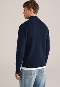 Mörkblå stickad tröja med hög krage, texturerad tyg, ribbade ärmslut och fåll, kombinerad med ljusblå jeans.