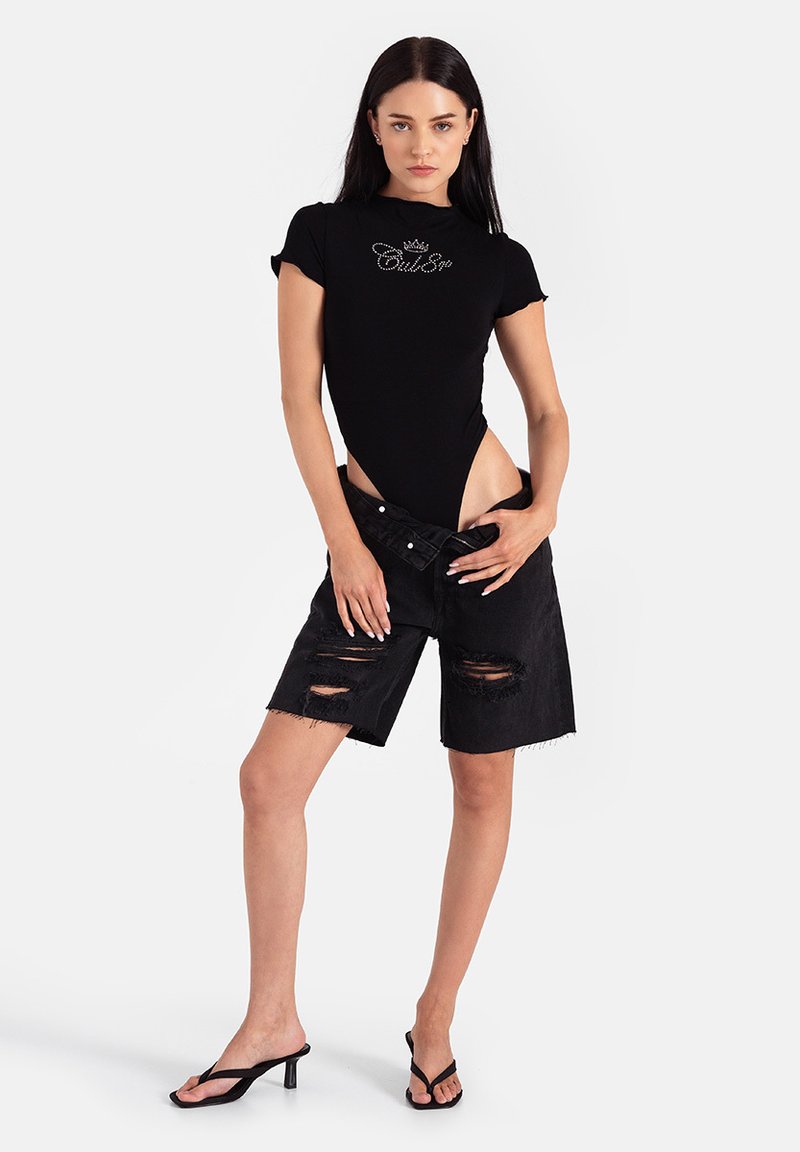 Czarny body z krótkimi rękawami i logo z kryształków, w zestawieniu z czarnymi, postrzępionymi szortami dżinsowymi. Modelka ma na sobie czarne klapki.
