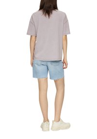 T-shirt oversize lilas clair à manches courtes, associé à un short en denim bleu clair avec des bords effilochés et des poches. Baskets blanches.