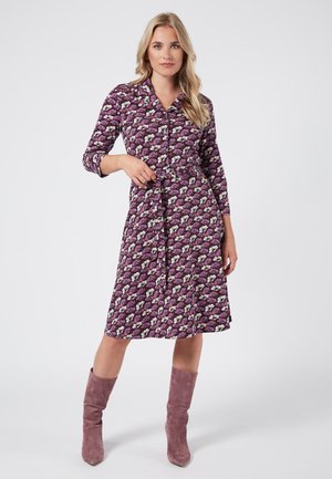 Lila Blumenkleid mit Knopfleiste, gefettetem Taillenbereich und drei Viertelärmeln. Kombiniert mit rosa Knöchelstiefeln.
