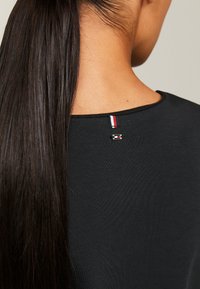 Zwarte T-shirt met een ronde halslijn, een soepele textuur en een klein driekleurig label met rode, witte en blauwe strepen aan de achterkant.