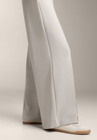 Ljusgrå vida byxor i mjukt tyg, med en ren sömdesign. Matchas med vita sneakers som har en texturerad sula.