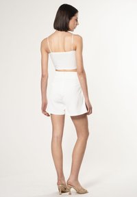 Top bianco a fascia corta con spalline sottili, abbinato a pantaloni corti bianchi a vita alta. Tessuto liscio con un design pulito. Tacchi aperti in tono neutro.