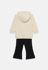 Felpa in cotone beige con cappuccio e maniche lunghe, abbinata a leggings neri a zampa d'elefante. Texture morbida, design casual e senza fantasie visibili.