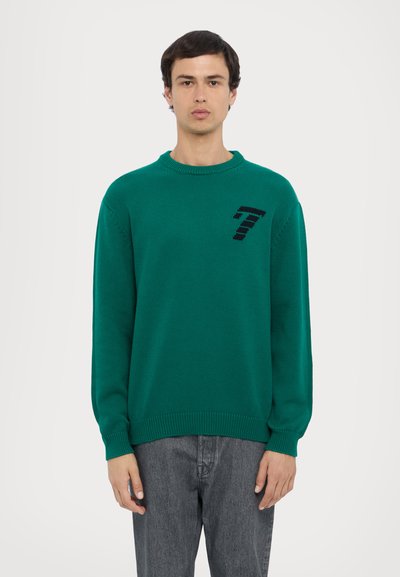 Pull en tricot vert avec un col rond, des manches longues et un design noir avec le numéro 7 sur la poitrine ; finition texturée et poignets côtelés.