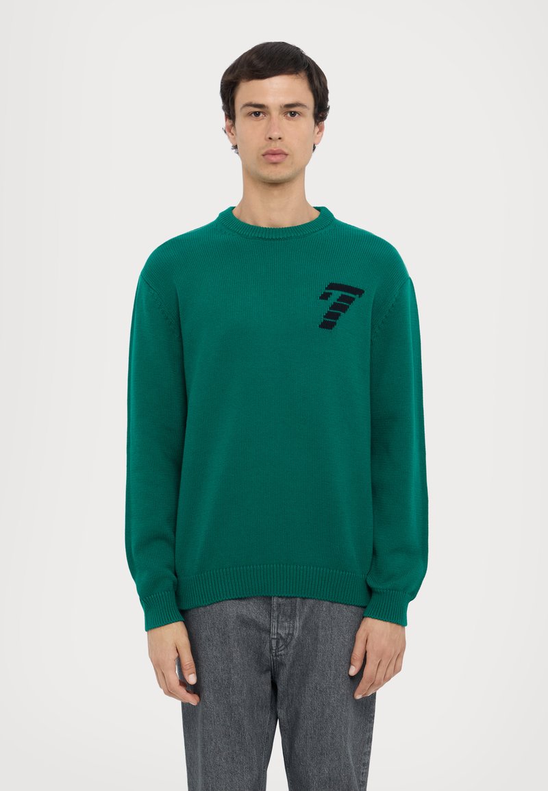 Pull en tricot vert avec un col rond, des manches longues et un design noir avec le numéro 7 sur la poitrine ; finition texturée et poignets côtelés.