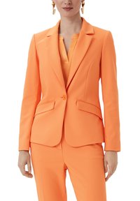 Oranger maßgeschneiderter Blazer mit einem einzigen Knopfverschluss, Reverskragen und zwei Vorderaschen. Hergestellt aus glattem Stoff, kombiniert mit einem passenden Outfit.