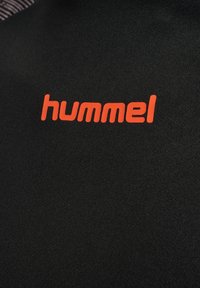 Zwarte stoffen materiaal met het woord "hummel" prominent weergegeven in feloranje, met een soepele textuur zonder merkbare patronen.