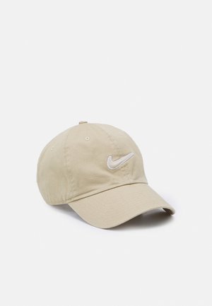 Beżowa czapka bejsbolowa Nike z zakrzywionym daszkiem i białym, haftowanym logo Swoosh z przodu, prezentowana na białym tle.