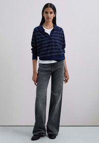 Navy striped sweater with a polo collar, paired with gray wide-leg jeans and textured black shoes. Model wearing a silver chain necklace.
