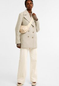 Beige villa-sekoitusta oleva kaksirivinen takki suurilla napilla, yhdistettynä vaaleancremeihin leveälahkeisiin housuihin ja vaaleanbeigeen crossbody-laukkuun, jossa on pehmeä tekstuuri.