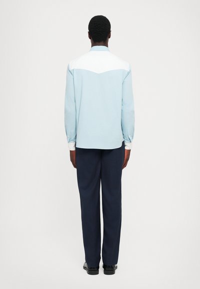 Cămașă bleu deschis, cu umeri albi, asortată cu pantaloni negri închis. Croială slim, mâneci lungi cu butoni la manșete, textură de țesătură netedă.