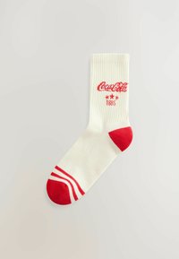 Valge puuvillane sokk punaste varba- ja kannaaktsentidega, punaste triipudega kummil, ning tikitud "Coca-Cola" logo koos tähtede ja aastaga "1886."
