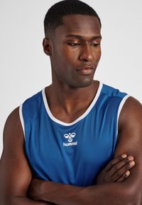 Blauwe mouwloze sportshirt met witte rand, met een logo op de borst. Het materiaal lijkt glad en lichtgewicht te zijn.