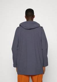 Manteau imperméable bleu marine avec capuche, de coupe droite et manches longues, fabriqué dans un tissu lisse et mat.