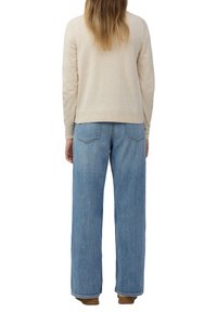 Beige trui met ribbelzoom, gecombineerd met lichtblauwe wijde jeans met achterzakken en een vervaagde denimtextuur.