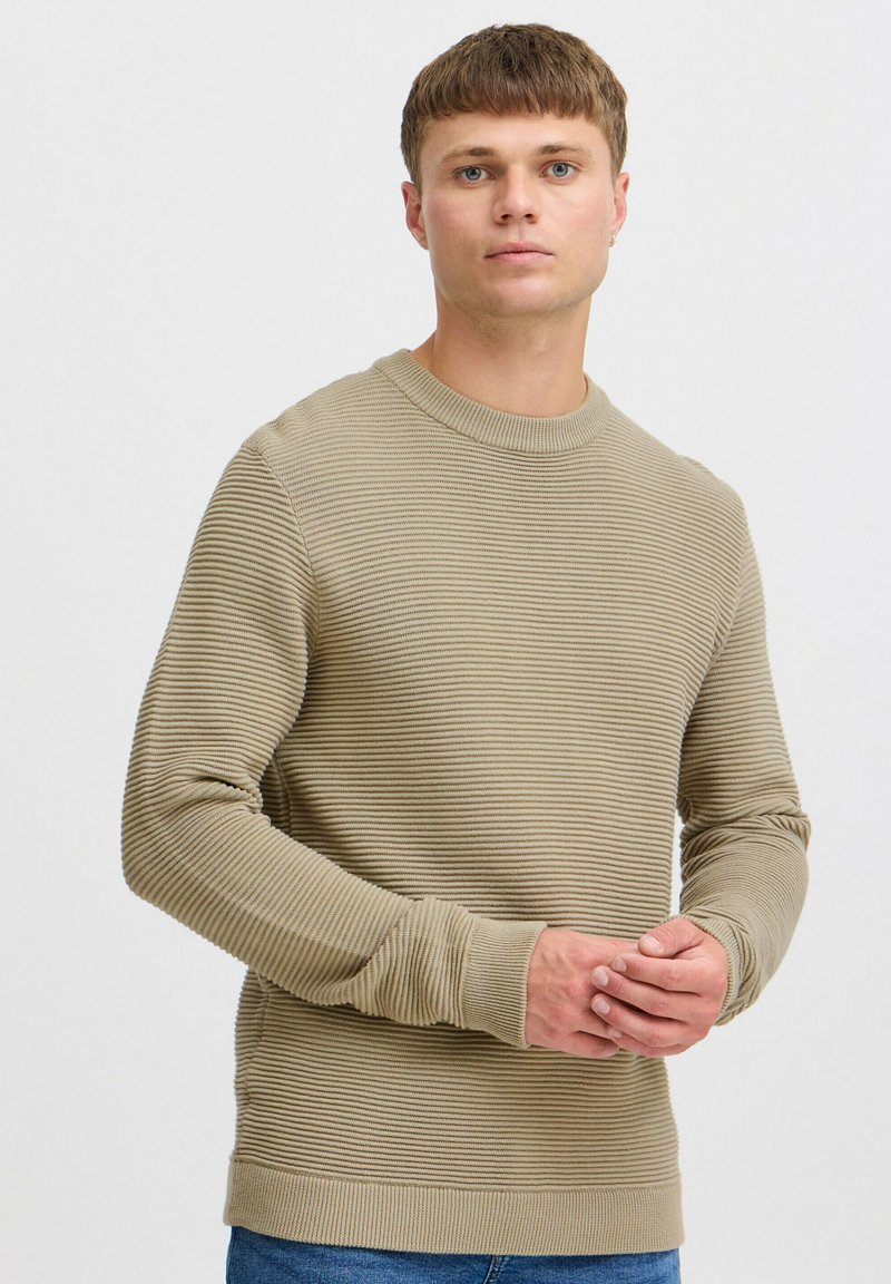 Beige geribde gebreide trui met een ronde halslijn, lange mouwen en een textuurpatroon. Heeft aansluitende boorden en een zoom.