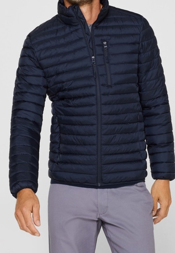 Mørkeblå puff jakke med vandret syninger, høj krave, frontlynlås og en lynlåslomme på brystet. Letvægts og quiltede design.