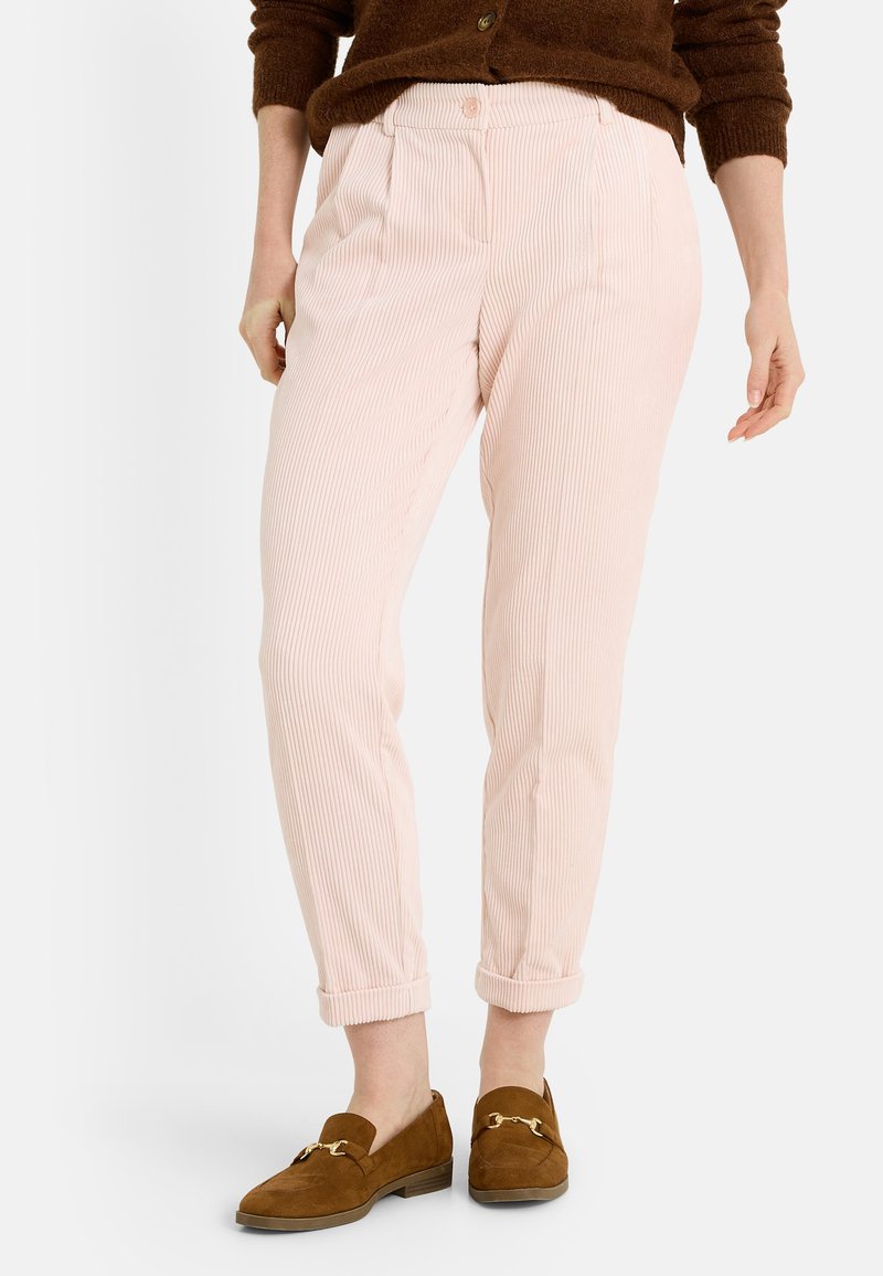 Pantalones de pana rosa claro con un corte holgado, que incluyen un frente plisado y puños enrollados, combinados con zapatos de ante marrón.