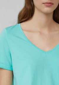 Turkusowa koszulka z dekoltem w serek i krótkimi rękawami, wykonana z miękkiej bawełny. Charakteryzuje się gładką fakturą i czystym cięciem przy dekolcie i rękawach.